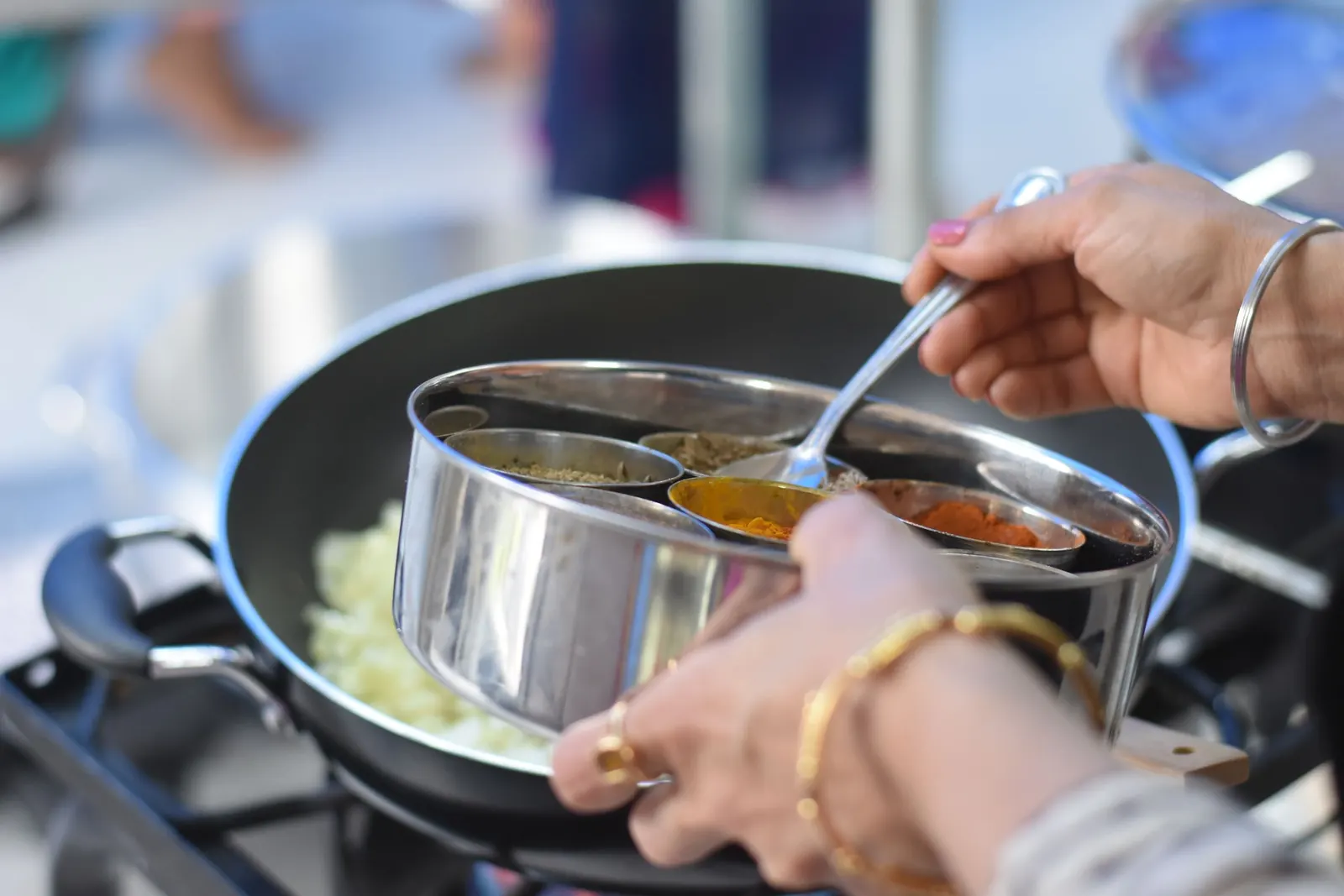 Hands serving curry from a steel tiffin at a home stove